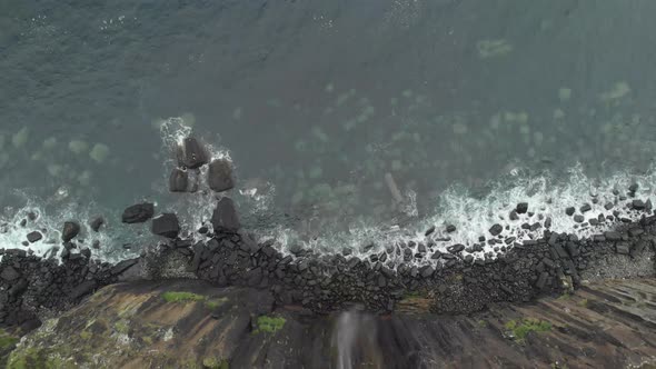 Drone reveal shot of a waterfall ending in a sea cliff in isle of skye scotland. Clear blue water an