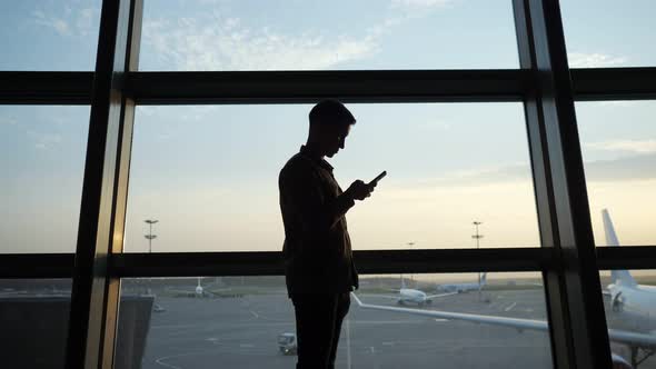 Man Surfs Internet with Smartphone Near Window at Airport