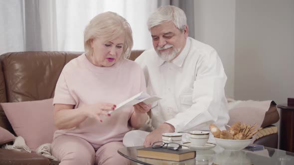 Anxious Senior Caucasian Woman Opening Letter and Touching Face with Hand, Hansome Old Husband