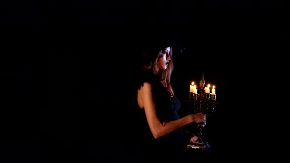 Young Sexy Witch Blows Out the Candles on a Black Background