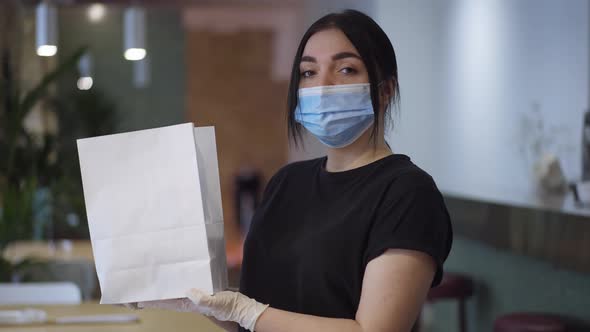 Waitress in Coronavirus Face Mask Standing with Packed Lunch Turning Looking at Camera