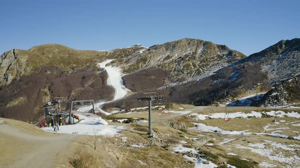 Aerial, Alps Mountains Partially Covered With Snow In Italy And A Chairlift With Skiers
