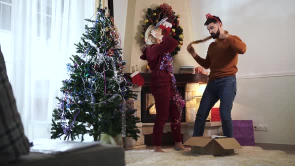 Young Caucasian Girl with Blond Hair Putting Happy New Year Headband on Husband's Head. Cheerful