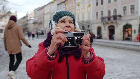 Senior Old Woman Tourist Taking Pictures with Photo Camera Using Retro Device in Winter City Center