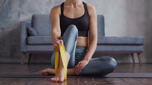 Young and sporty girl in sportswear is doing exercises in home interior using resistance band.