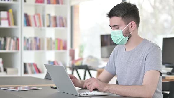 Cautious Young Man with Face Mask Using Laptop