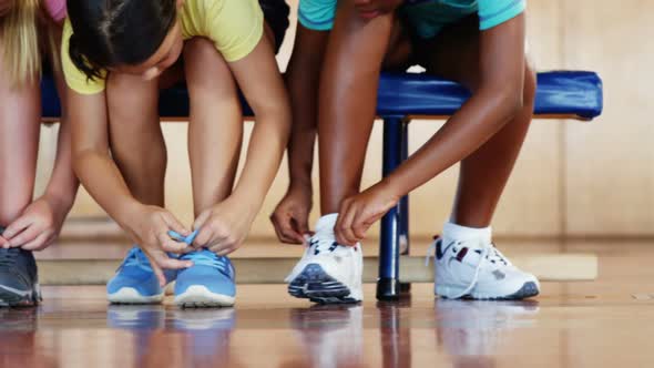 Girls tying shoe laces in basketball court