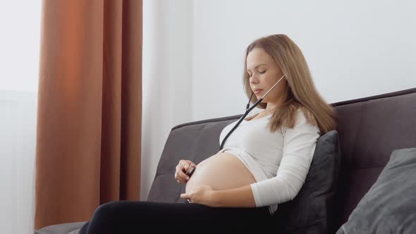 A Pregnant Fairskinned Woman Listens to the Movements and Heartbeat of the Fetus with a Stethoscope