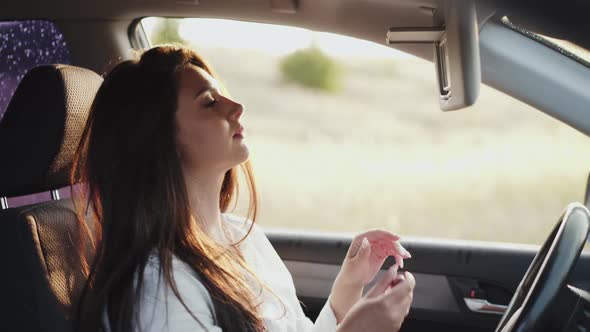 Pretty Longhaired Girl Applying Lipstick at Car Front Mirror