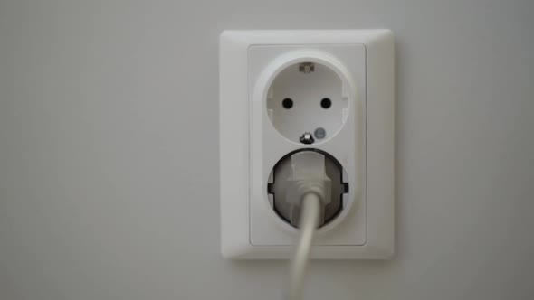 Female Hand Puts a Power Plugs in the Wall Socket