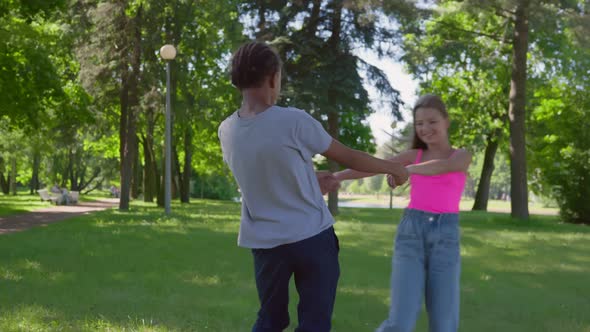 Teenage African Boy and Caucasian Girl Holding Hands and Dancing in Circle Together Outdoors