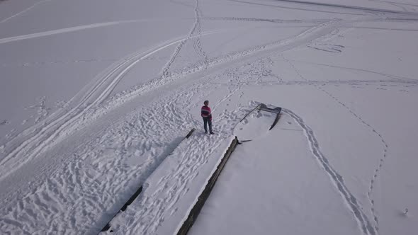 Slow panning aerial footage of blonde female standing on edge of wooden jetty staring over frozen la