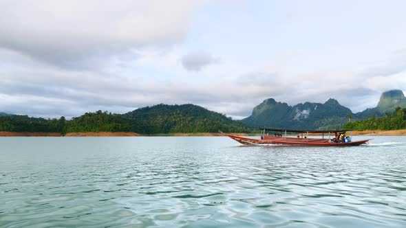 Traditional Wooden Boat Sailing on Blue Lake with Green Rain Forest Mountains