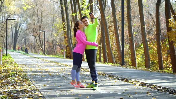 Cheerful couple in love posing for selfie after jogging in autumn park