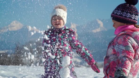 Cheerful Little Girls in Outwear Having Fun and Throwing Snow in Sunlight Standing Outdoors