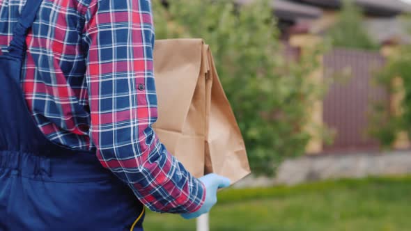 Rear View: A Delivery Service Employee Carries Food Bags To the Customer's Home