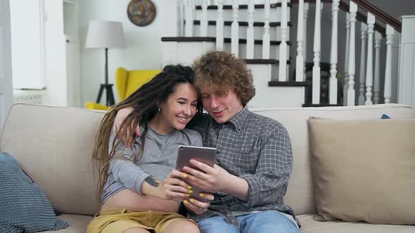 Preganat Couple in Love Sitting on the Soft Couch in the Living-Room and Looking Photo on I-pad