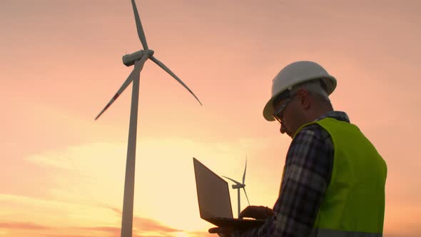 Windmill Engineer Watching Wind Turbines in Operation on a Laptop
