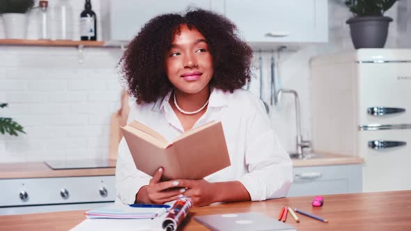 Young African American Woman Student Reading Textbook and Looking Up Dreamily