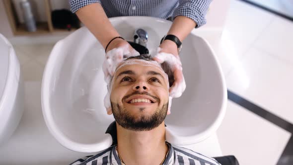 Happy Charismatic Young Man at the Barber Shop While the Man Washes His Hair