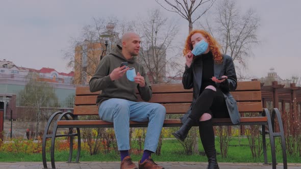 Man and Woman Sitting on Park Bench Take Off Their Protective Masks and Begin to Communicate