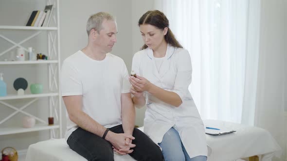 Young Beautiful Caucasian Doctor Giving Medical Drops To Mid-adult Man in Hospital Ward. Portrait of