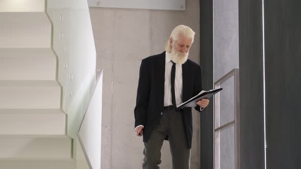 Senior Man in Suite with Notepad Going Downstairs in a Building