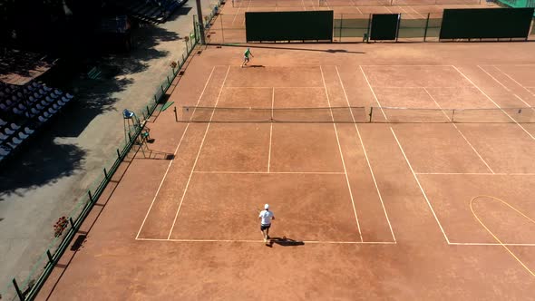 Tennis clay court seen from above with two men playing match. They are mature adult