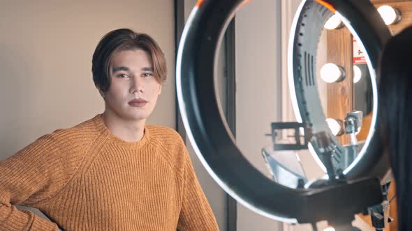 A Guy with Bold Nude Lips Sitting in Makeup Studio - the Artist Taking Photos of Him on Her Phone