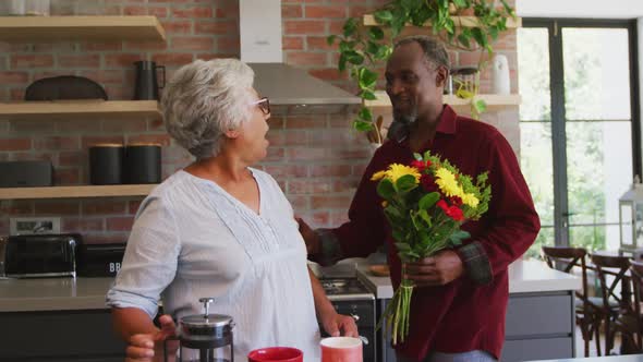 Senior African American husband offering flowers to his wife, hugging and smiling