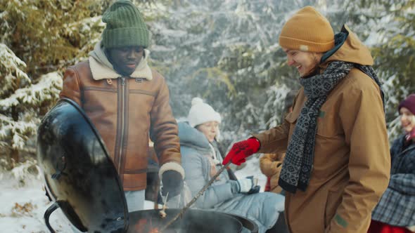 Men Eating and Chatting by BBQ Grill on Winter Picnic in Woods