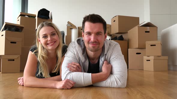 A Happy Moving Couple Lies on the Floor of an Empty Apartment and Smiles at the Camera