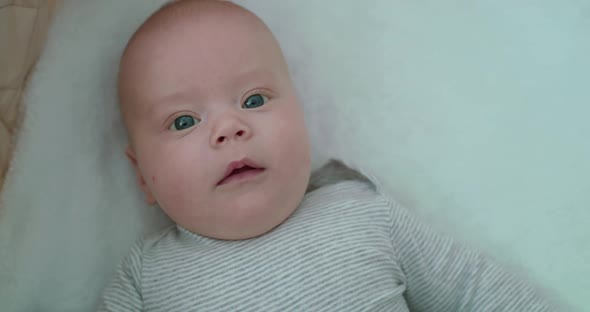 Perplexed Newborn Baby Lying in Bed and Looking at Camera