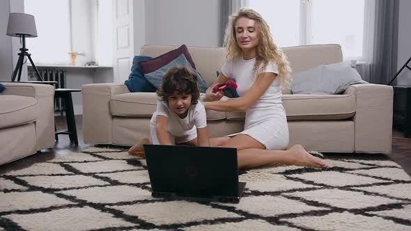  Lovely Mother and Son Sitting on the Carpet Near the Couch and Playing Video Game on Computer