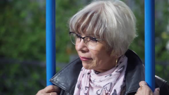 Headshot Portrait Sad Senior Caucasian Woman Swinging on Swing on Playground Outdoors in Sunshine