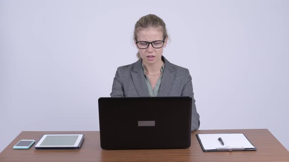 Young Confused Blonde Businesswoman Using Laptop and Shrugging Shoulders at Work