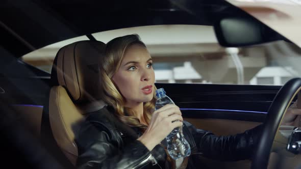 The girl behind the wheel drinks water.