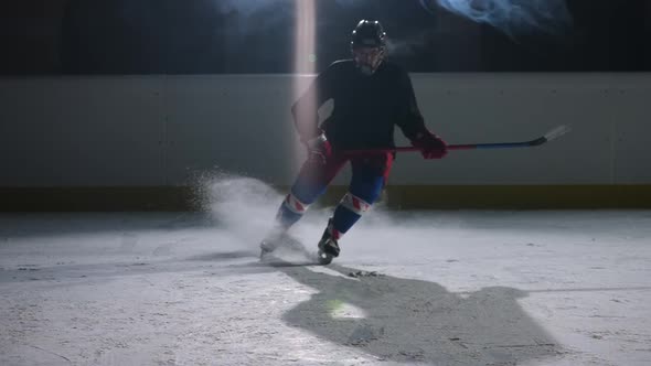 Hockey Player Slides Across a Dark Ice Arena with Spotlights and Smoke Hits the Ice with a Hockey