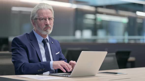 Thumbs Down By Old Businessman with Laptop at Work