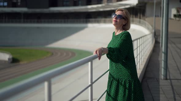 Attractive Confident Caucasian Woman Standing in City Looking Up at Sunlight in Sunglasses