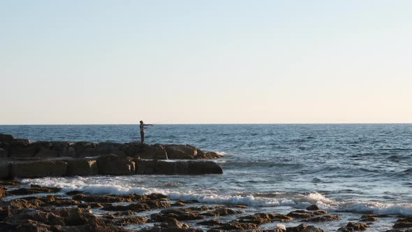 Fisherman Standing on Rocky Shore Pier and Catching Fish