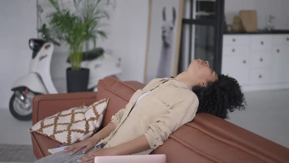 Side View of Tired African American Woman Leaning on Couch in Home Office