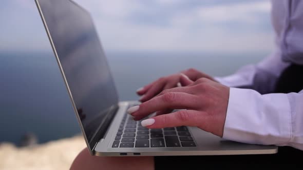 Well Looking Middle Aged Woman Typing on Laptop Keyboard Outdoors on Terrace with Beautiful Sea View