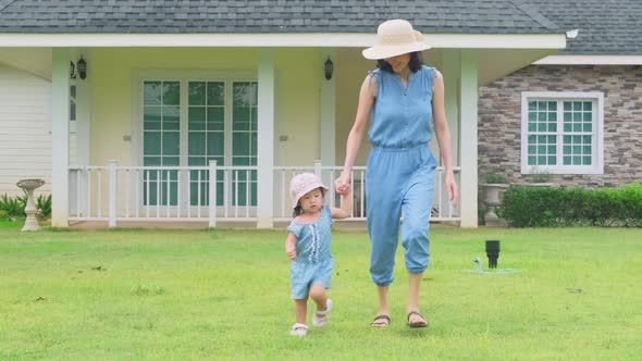 Asian family having fun together at home. Mother holding child hand walking outdoor in garden. alt
