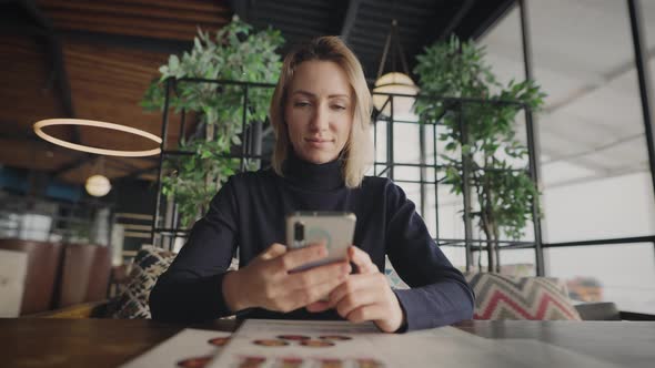 Attractive Blonde Woman Uses a Smartphone in a Cafe