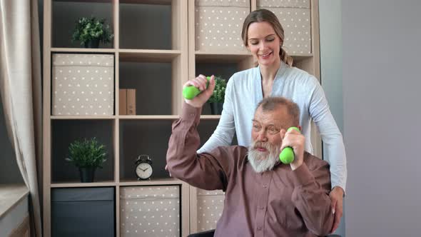 Happy Woman Doctor Rehabilitation Disabled Elderly Man Exercising with Dumbbells at Wheelchair