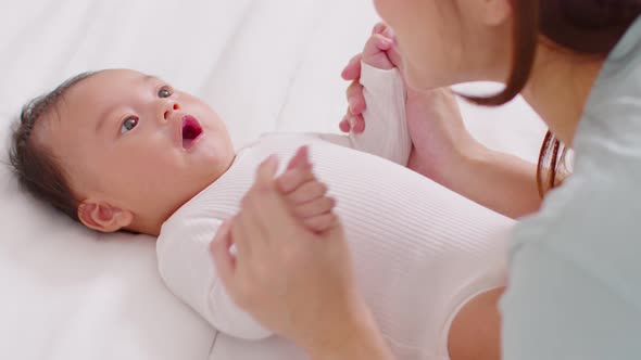 New asian mom playing to adorable newborn baby on bed