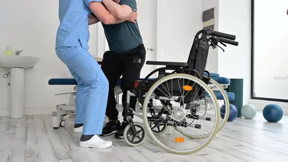 Male Physiotherapist Helping a Patient with a Neurological Disease to Get Up From Wheelchair at