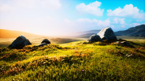 Meadow with Huge Stones Among the Grass on the Hillside at Sunset