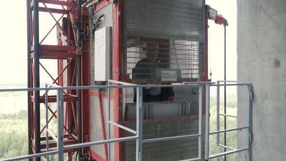 A Man Builder Closes the Doors of the Cargo Construction Elevator and Moves Down